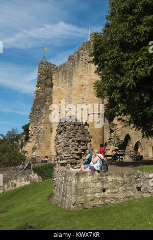 People sitting on benches relax & enjoy summer sun, near medieval tower keep & ruins of Knaresborough Castle beyond - North Yorkshire, England, UK. Stock Photo