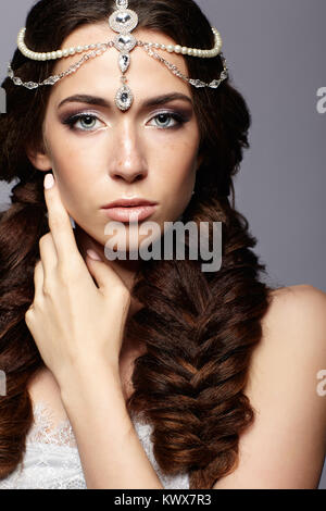 Beauty portrait of young woman with diadem. Brunette girl with long hair plaits and day female makeup on gray background. Stock Photo