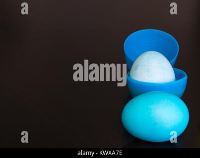 A blue plastic Easter egg is filled with a dyed egg. Another blue egg is in front of the filled egg. There is copy space left in the image. Stock Photo
