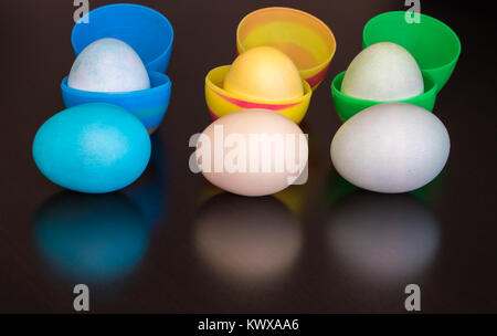 Three plastic Easter eggs are filled with dyed eggs. Three dyed eggs of the same color are infront of the filled eggs.  A reflecion is seen in the bla Stock Photo