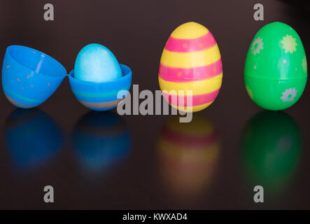 Three plastic Easter eggs are on a reflective table. 1 egg is opened and filled with a dyed egg. Reflections are cast on to the table. Stock Photo