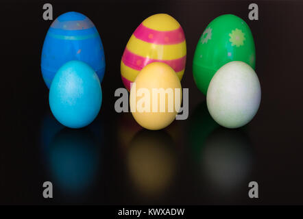 Three plastic Easter eggs are placed on a shiny table. Three dyed eggs are in front of the plastic eggs. Stock Photo