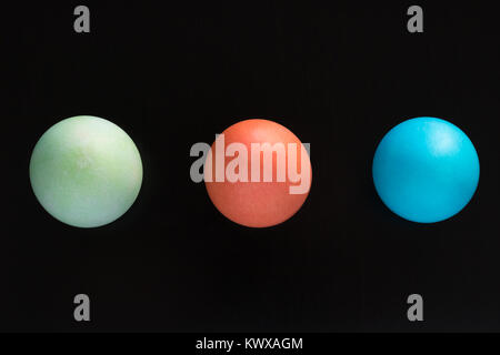 Three Easter eggs are on a black surface and viewed from above. They are green, red, and blue. Stock Photo
