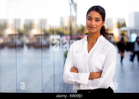 Beautiful female corporate executive modern business woman standing arms folded outside work at office building Stock Photo