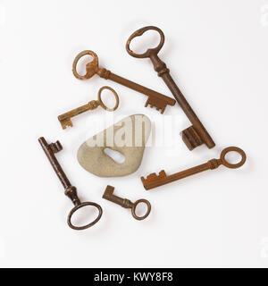 set of old rusty keys placed around grey stone with key hole on white background  - concept of choice Stock Photo