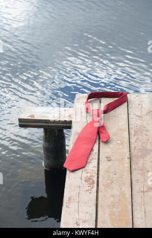 Concept with red necktie lying on wooden pier on background with river Stock Photo