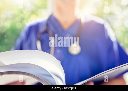 Doctor in scrubs uniform reading patient notes or medical chart Stock Photo