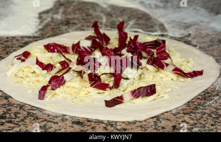 Fresh original Italian raw pizza, dough preparation in traditional style,with cheese and red chicory. Food, italian cuisine and cooking concept. Stock Photo