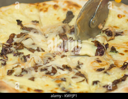 Closeup hand of chef baker cutting pizza at kitchen. Food, italian cuisine and cooking concept. Stock Photo