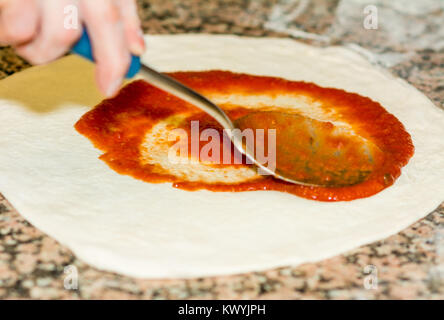 Fresh original Italian raw pizza, dough preparation in traditional style. the chef spreads the tomato sauce. Food, italian cuisine and cooking concept Stock Photo