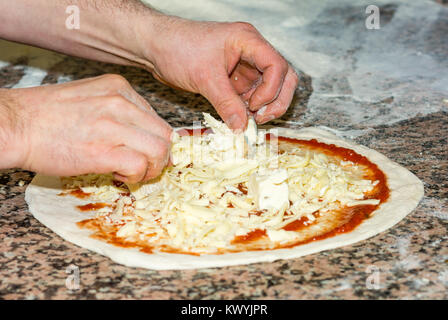 Fresh original Italian raw pizza, dough preparation in traditional style: the chef distributes the cheese. Food, italian cuisine and cooking concept. Stock Photo