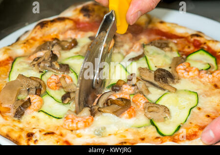 Closeup hand of chef baker cutting pizza at kitchen. Food, italian cuisine and cooking concept. Stock Photo