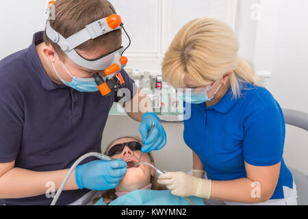 Dentist in mask with loupe binoculars and assistant working on patient. Madical office Stock Photo
