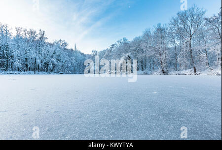 Bright winter scene of frozen pond and trees covered in snow in United Kingdom Stock Photo