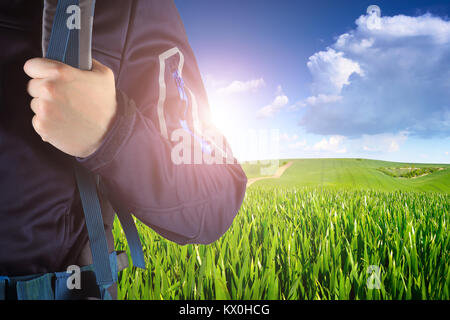 Tourist hand on backpack close-up. Hiker on summer sunrise background. Bright tourism concept. Good travel theme. Stock Photo