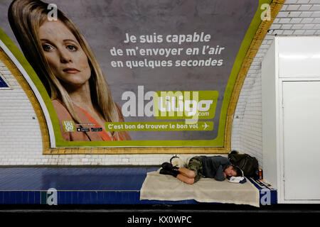 France, Paris, Man sleeping in metro station under an advertisement that says 'I am capable of getting myself a flight in a few seconds'. Stock Photo