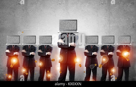 Businessmen in suits with laptops instead of their heads keeping arms crossed while standing in a row among flying lightulbs in empty room with gray w Stock Photo