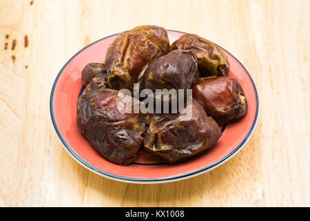 Dried dates fruit in a red plate on a wooden board Stock Photo