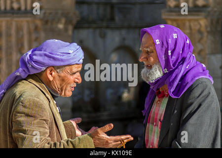 Local elderly men talking to each other in Sanliurfa, Turkey. They wear traditional purple headdress. Stock Photo