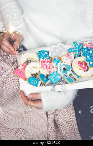 Woman hands holds a white plate with decorated winter/christmas cookies and a sparkle Stock Photo