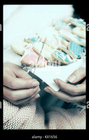 Woman hands holds a white plate with decorated winter/christmas cookies and a sparkle Stock Photo