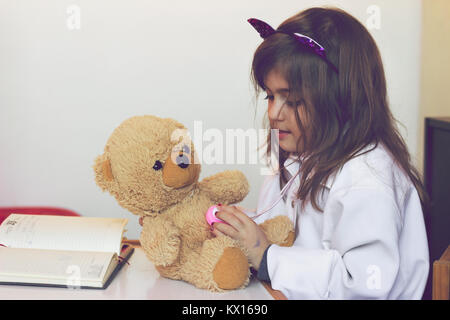 Little girl pretends to be a doctor and playing with her teddy bear Stock Photo