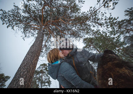 Young couple in love with dog walking in the snowy pine forest and kissing Stock Photo