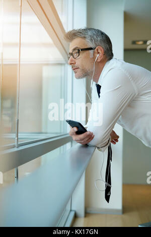 Businessman talking on phone in office, standing by window Stock Photo
