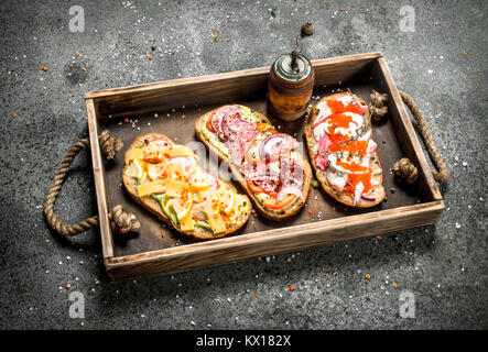 Various sandwiches with seafood, meat and vegetables on an old tray. On a rustic background. Stock Photo