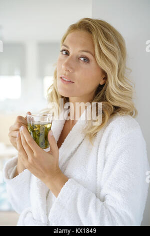 Portrait of attractive 40-year-old woman in bathrobe drinking infusion Stock Photo
