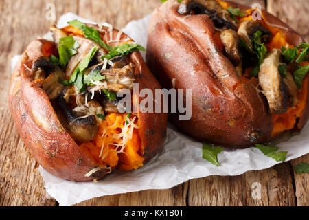 Organic baked sweet potato with mushrooms, herbs and cheese close-up on parchment on the table. horizontal Stock Photo