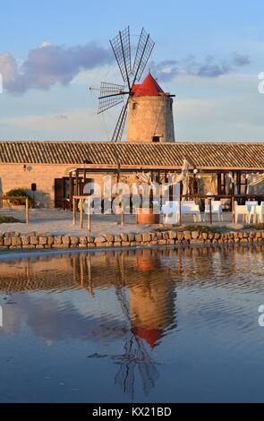 One of the traditional windmills in the salt flats of Trapani, Sicily (Italy) reflected in a salt basin. Stock Photo