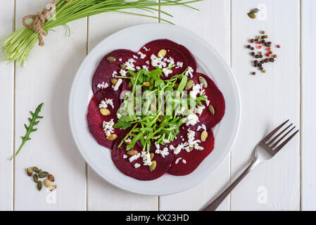 Beetroot carpaccio with rucola leaves and pumpkin seeds on wooden white background. Stock Photo