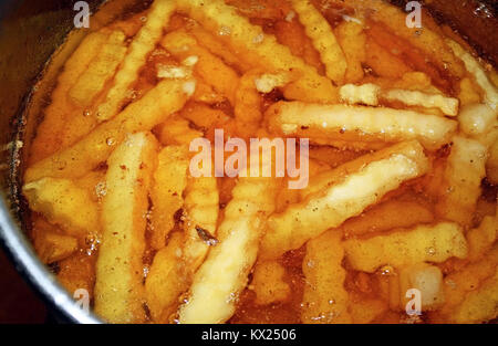 Crinkle Cut french fries sitting in a pot of oil in deep fryer Stock Photo