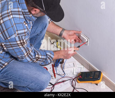 Electrician uses insulated screwdriver to mount electrical outlet plate. Stock Photo