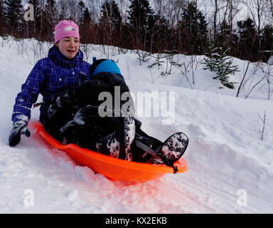 A teenager (18 yr old) in a sledge with a young child (5 yr old), looking nervous as its much faster than she thought Stock Photo
