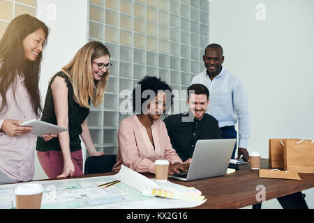 Smiling group of diverse businesspeople talking while working together around a desk in a modern office Stock Photo