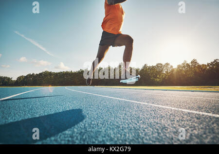 Fit young African male athlete in mid air while sprinting alone down a running track on a sunny day Stock Photo