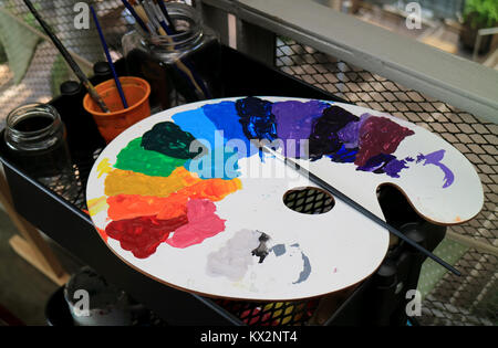 White art palette with multi-color paints and paintbrush on black tool cart Stock Photo