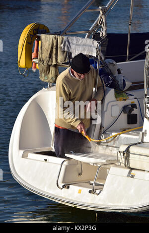 a man or a yachtsman using a yellow hose to clean his yacht. fresh water being used to hose down a boat to clean off the salt from sailing in the sea. Stock Photo