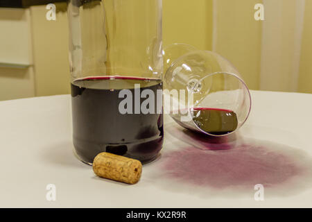 Red wine spilled from glass over white tablecloth with bottle and cork Stock Photo