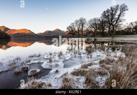 Warm sunlight rising over the Cumbrian fells and frozen lakes on a very cold still Winters morning. Stock Photo