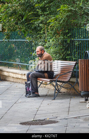 Typical down and out poor old man sitting on a roadside bench begging from passers by in Bucharest, capital city of Romania, central Europe Stock Photo
