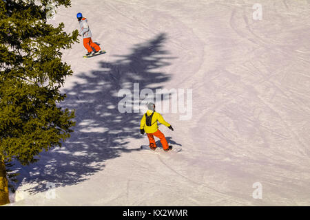 Young snowboarder going down a snowy slope, his instructor in front of him; view from above Stock Photo