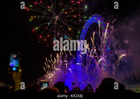 London, UK - January 1st 2018. Crowd of people watch and record with a  mobile phone the fireworks display at the London Eye to mark the end of 2017.