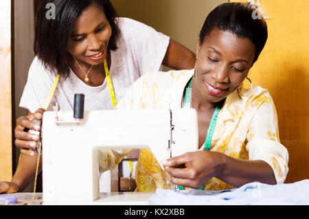 The professional seamstress sews and his trainee assists from behind. Stock Photo