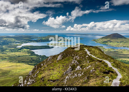 The hiking trail at the top of Diamond Hill in Connemara National Park, Ireland. Behind, the sun plays with the clouds reflected in the sea. Stock Photo