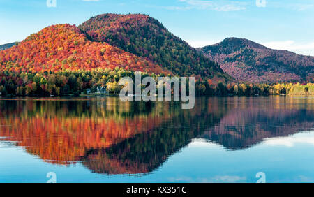 The hills covered with red maple forests are reflected in a lake in Quebec on a beautiful autumn evening Stock Photo