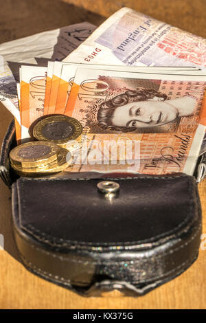 New £10 notes and £1 coins, pound / pounds sterling currency, on a leather purse. Concept of British / UK money, income, expenditure, capital, etc. Stock Photo