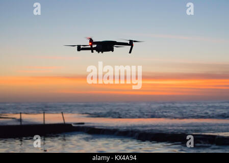A silhouetted drone flies low over an ocean pool near Sydney very early in the morning in Australia Stock Photo